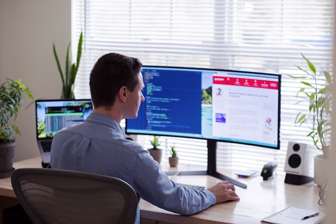 A man seated at a desk, working on two monitors displaying top RFP software applications.